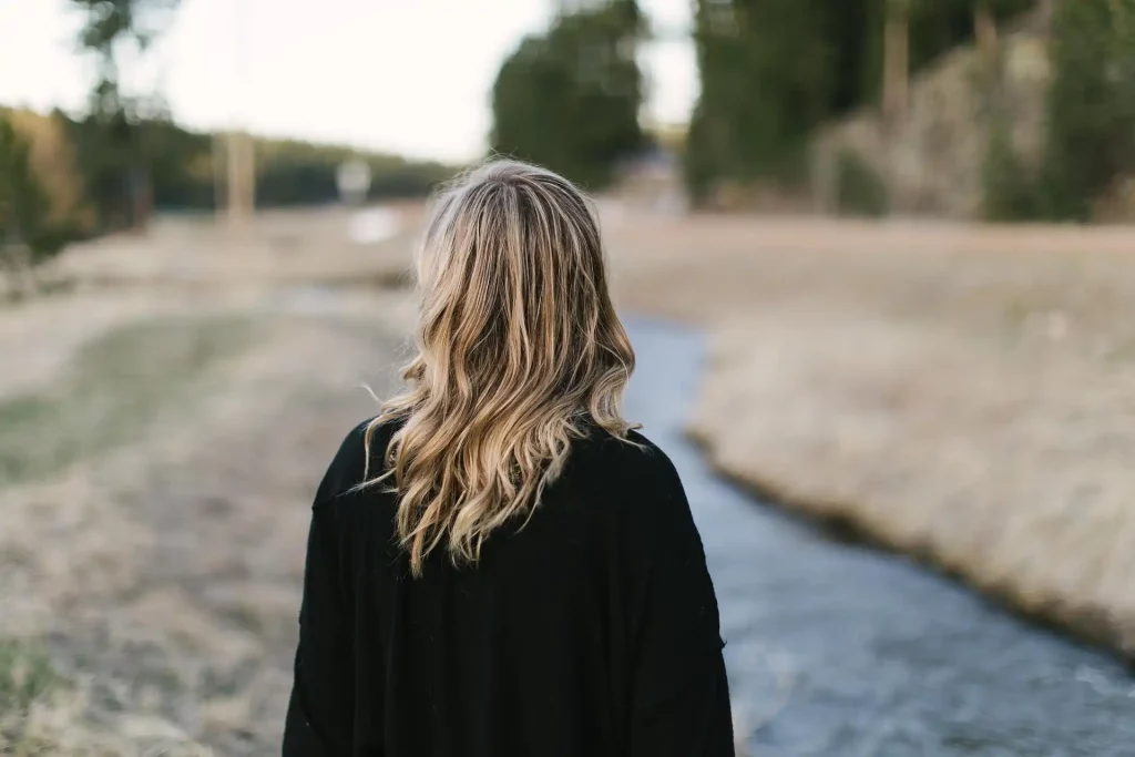 A woman walking away through a green field with a stream nearby. This relaxed image is a metaphor for the relaxed life coaching style that Fatima Sabeur uses at Magic Soul Coaching.